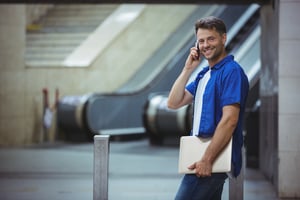 Handsome man holding laptop and talking on mobile phone at railway station