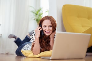 Attractive Young Woman Talking to Someone on Mobile Phone While Relaxing at the Living Room with Laptop Computer-1