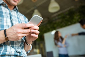 Closeup of hands of young man in checkered shirt using mobile phone while his partners arguing.jpeg