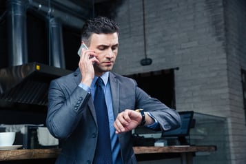 Confident businessman speaking on the phone and looking on the wristwatch in cafe.jpeg