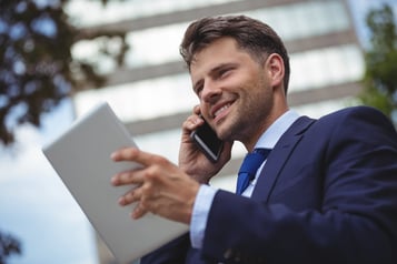 Handsome businessman holding digital tablet and talking on mobile phone.jpeg