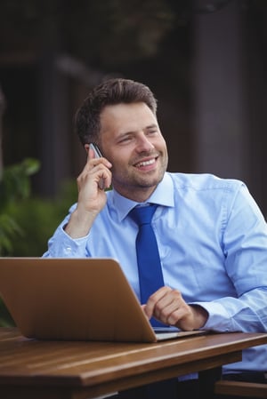 Handsome businessman talking on mobile phone while using laptop at outdoor cafx96xA7