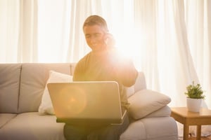 Happy man sitting on couch phoning and using laptop at home in the living room