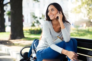 Portrait of a happy woman sitting on the bench and talking on the phone outdoors